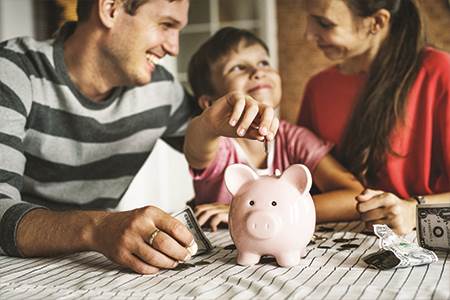 mom dad and son together talking about savings while child is putting money in piggy bank